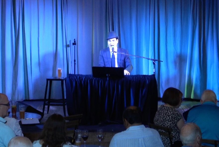 Pianist seated at a piano on stage in front of blue curtains.