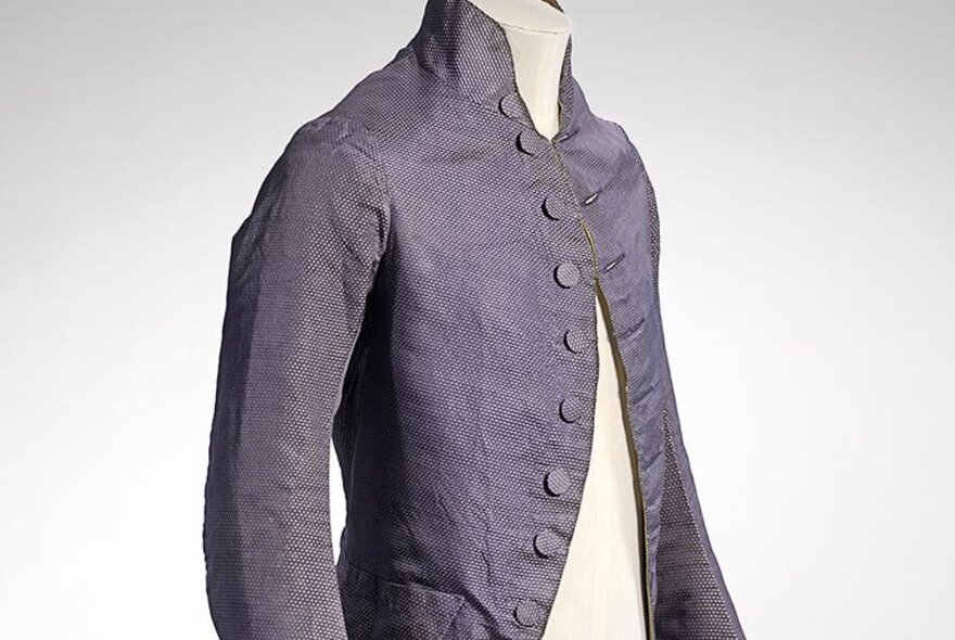 A dark blue figured silk coat from the 18th century on a cream fabric-covered mannequin.