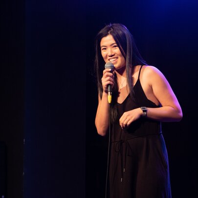 Performer wearing black in a dark venue, holding a microphone.