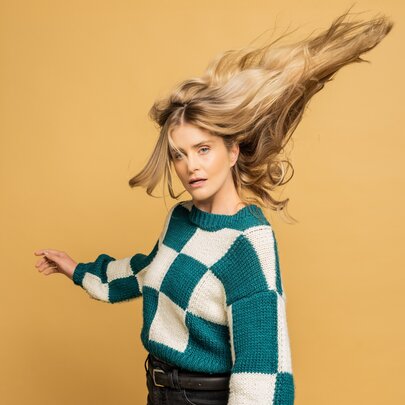 Comedian Amy Ruffle wearing a green and white checked jumper with her hair flowing out behind her.