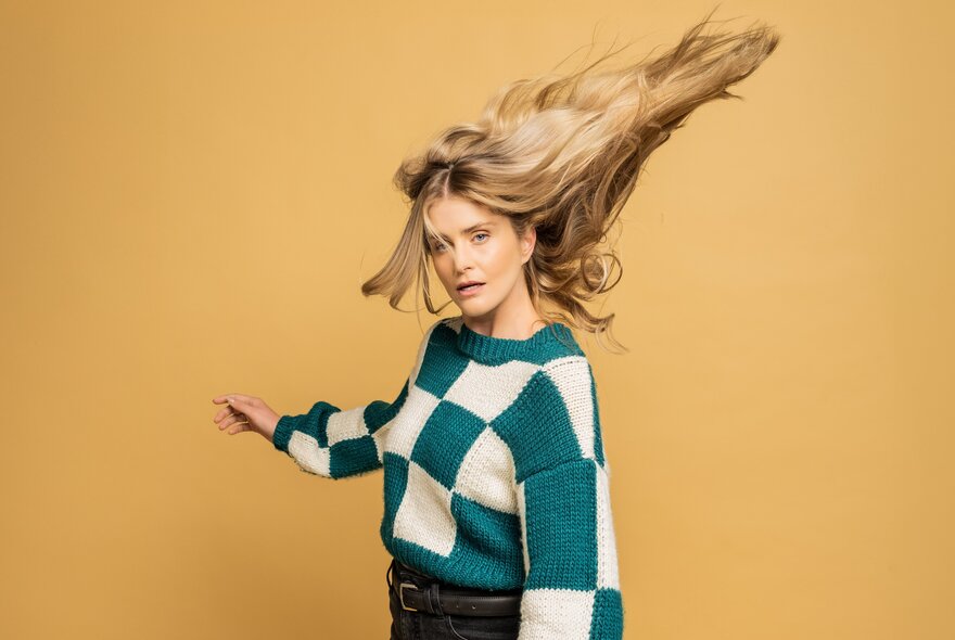 Comedian Amy Ruffle wearing a green and white checked jumper with her hair flowing out behind her.
