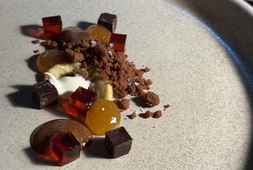 A deconstructed dessert featuring chocolate crumb and red jelly cubes.