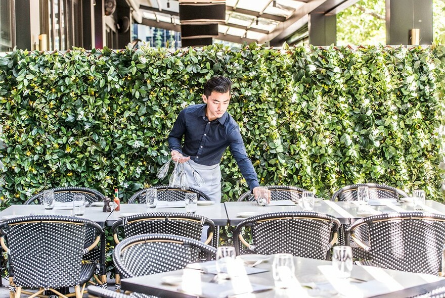 Waiter setting glasses on restaurant tables outdoors.