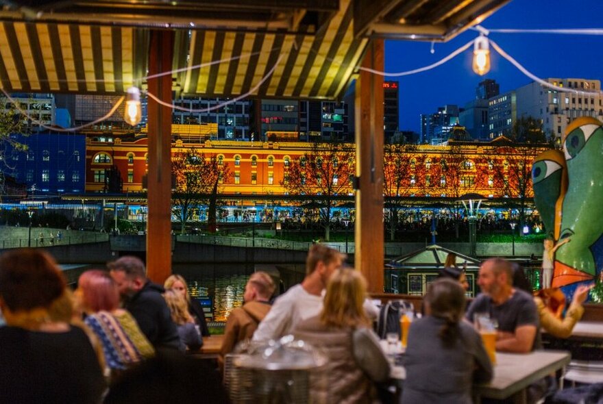 Customers and staff at restaurant tables overlooking city buildings at dusk.