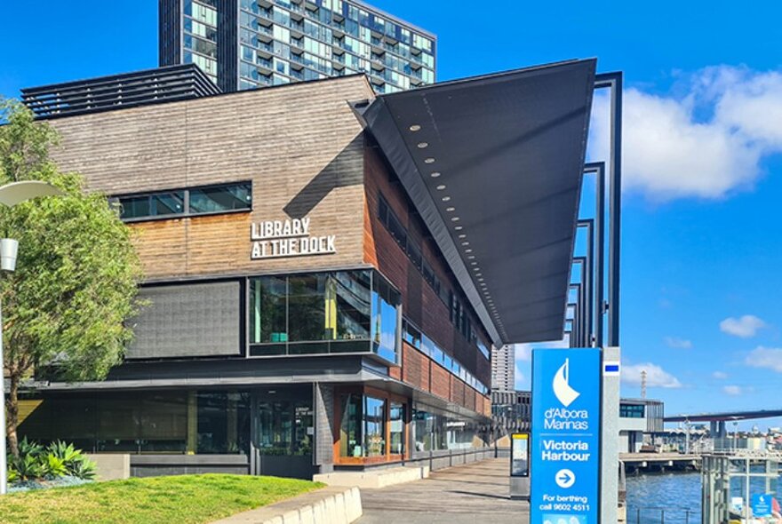 Architecturally designed Library at The Dock building with wood panel exterior and large windows and glimpses of the Yarra River.