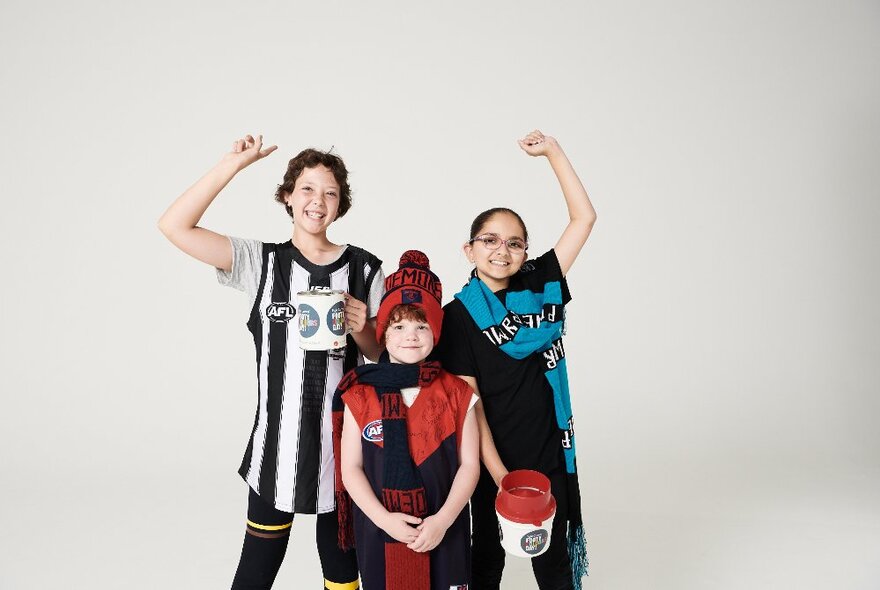 Three kids wearing footy colours, one holding on to a coin donation jug.