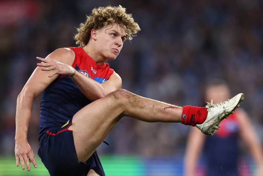 A Melbourne AFL football player kicking the ball during a match.