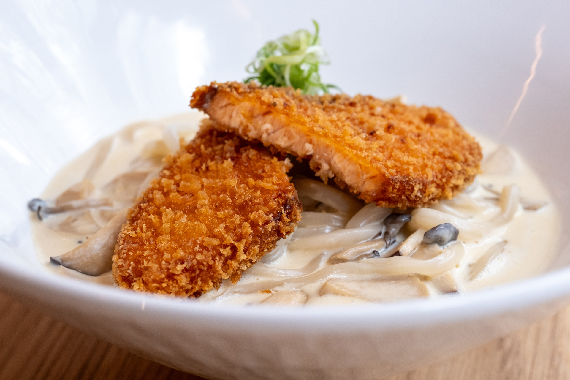 A bowl of carbonara udon noodles with crumbed salmon on top