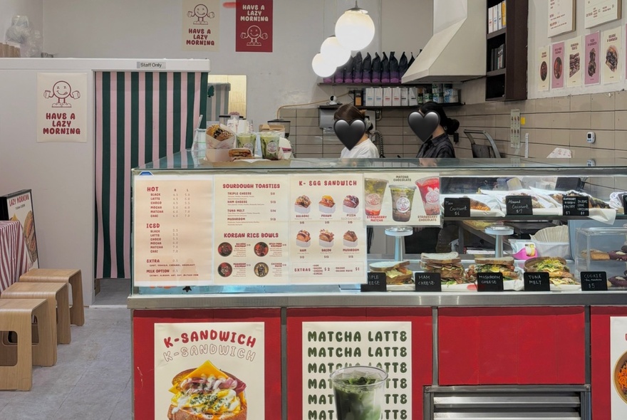 The glass counter and small kitchen of the takeaway shop Lazy Morning, with people preparing food in the kitchen.