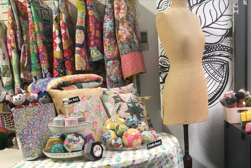Craft materials including a mannequin stand and hanging quilts.