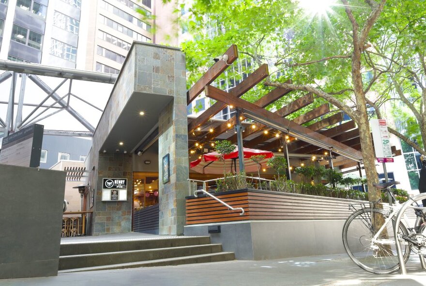 The exterior of Henry and the Fox restaurant showing the street entrance, stairs, green trees and an outdoor seating area.