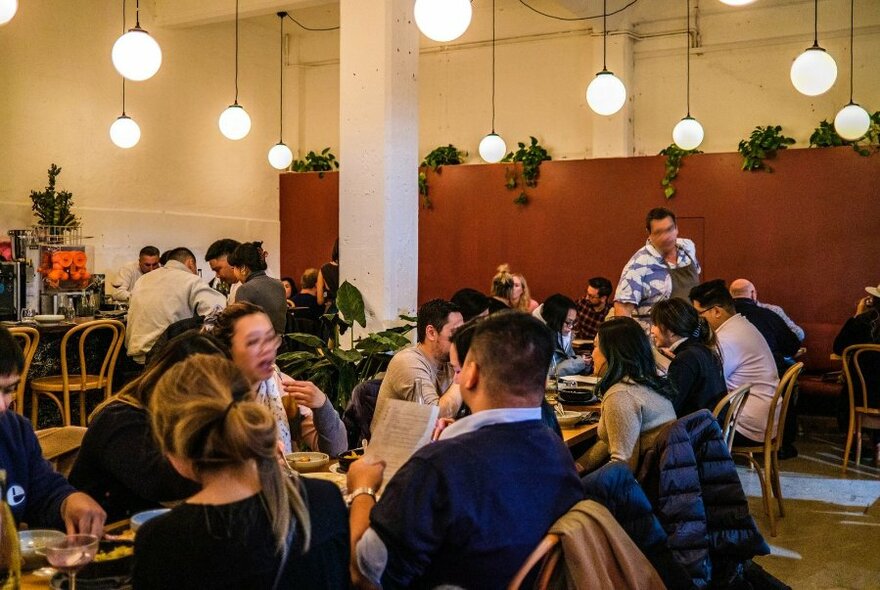 Restaurant interior with seated patrons dining at at tables, low round lights hanging from the ceiling.