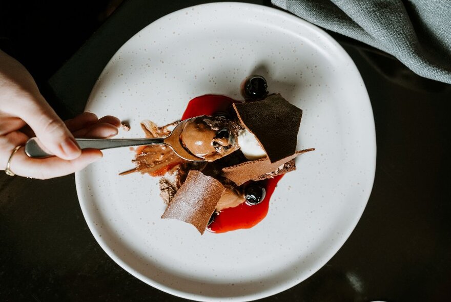 A hand holding a spoon of ice-cream over a plate of a dessert.