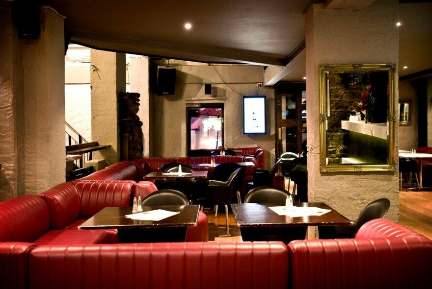 Red banquettes and tables in a white brick-lined room with mirrors and screens.