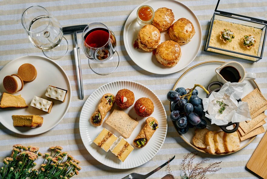 An array of cheese-themed savoury treats presented on white plates alongside wine glasses and grapes, seen from above.