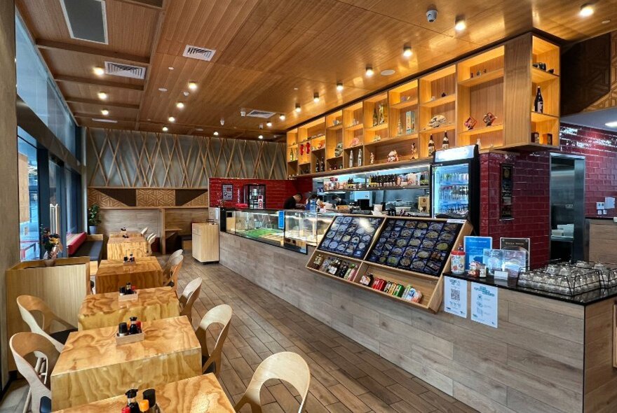 Interior of a Japanese restaurant with a long display counter and plywood tables and curved plastic chairs. 