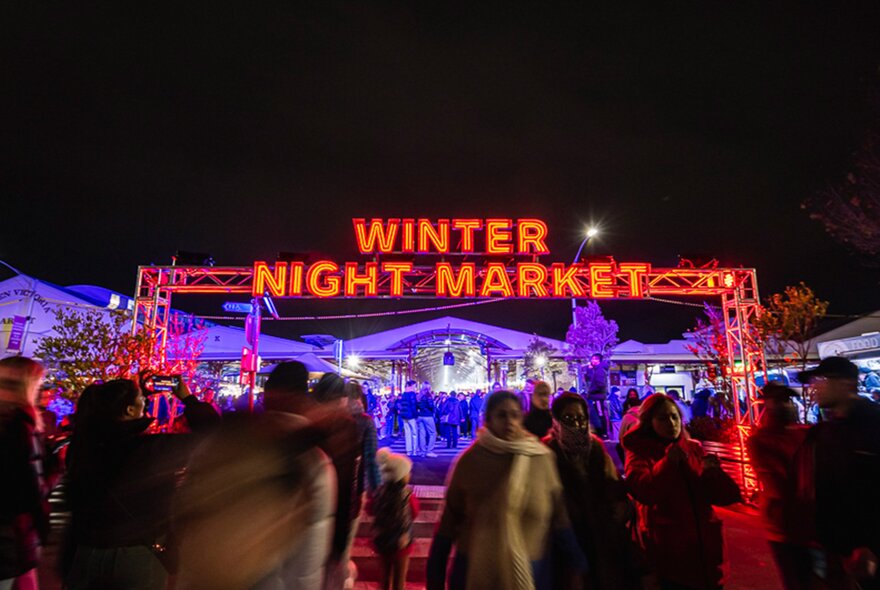 A crowd is walking under a glowing winter night market sign at night