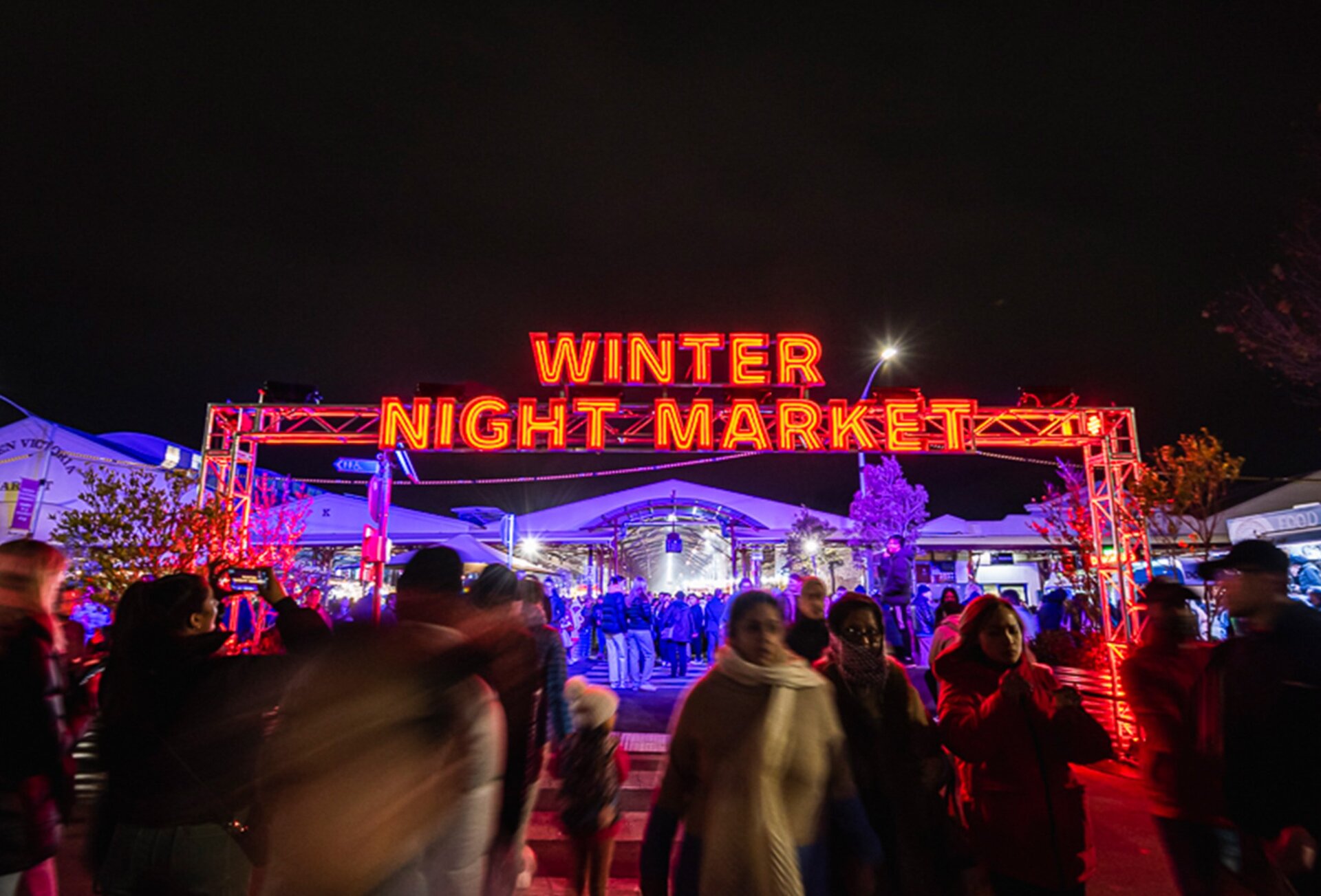 A crowd is walking under a glowing winter night market sign at night