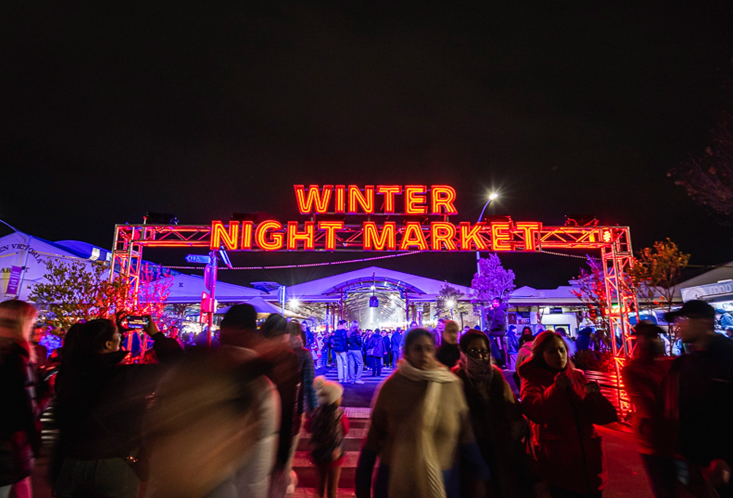 A crowd is walking under a glowing winter night market sign at night