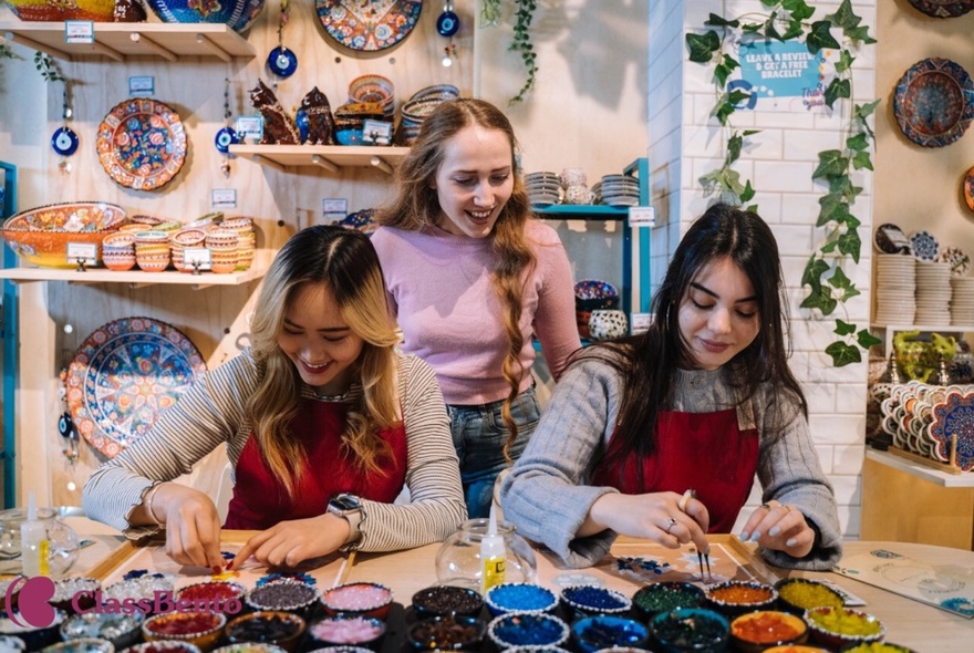 Two teenagers applying paint and mosaics in a workshop while another looks on.