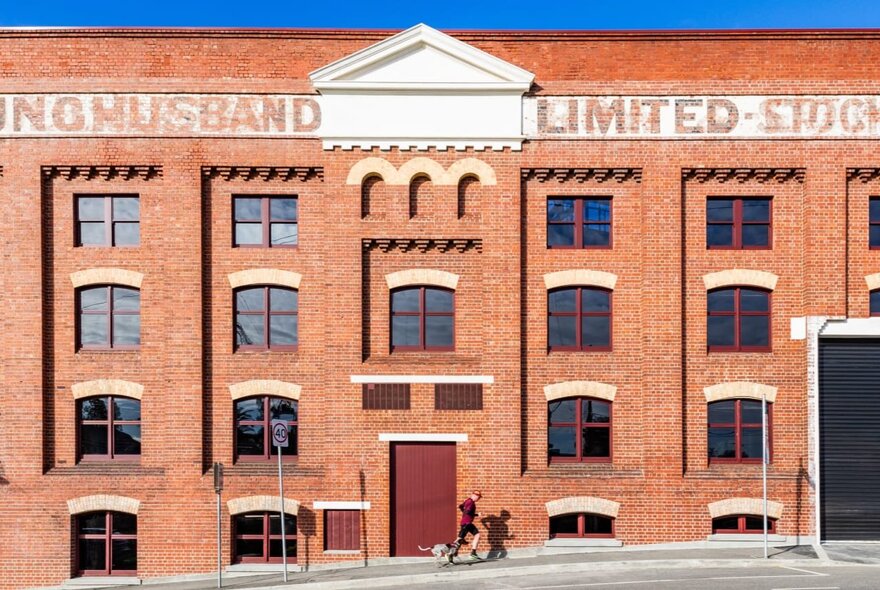 Old industrial red-brick warehouse with arched windows and central pediment.