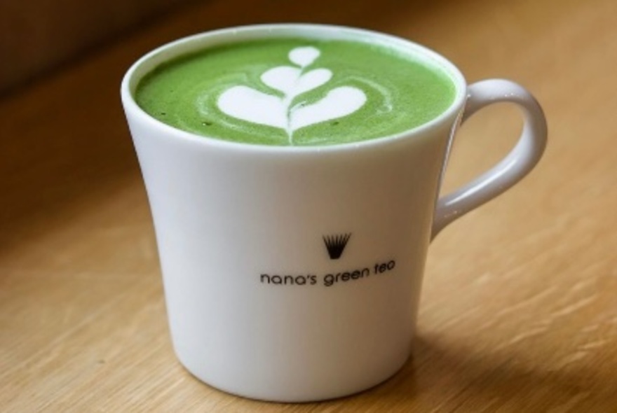 A matcha tea served in a white ceramic cup, on a wooden table.