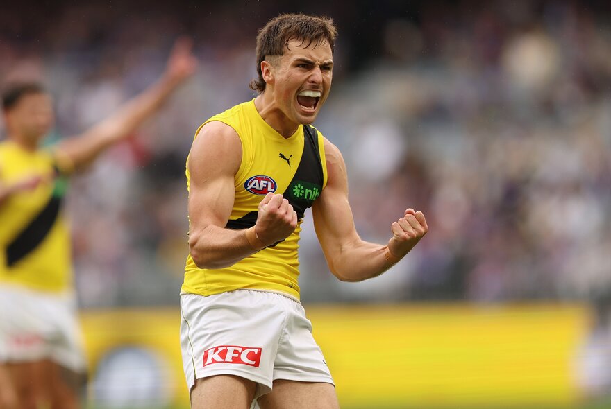 A Richmond AFL player celebrating on the field with his mouth open as if cheering, both his fists clenched.