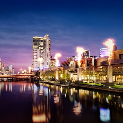 Crown Melbourne building illuminated at night by gas flares and reflections in Yarra River.