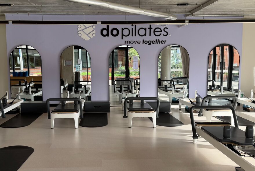 A reformer pilates studio with reformer beds and arched mirrors on a purple wall.
