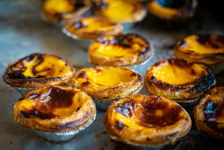 Portuguese tarts with blackened edges on a baking tray.