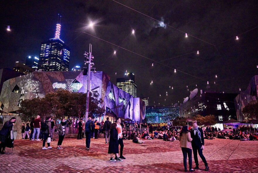 People milling around Fed Squre at night.