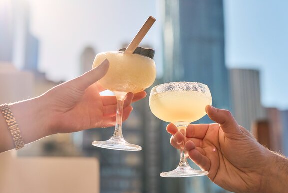 Two margaritas held in the sky in the city.