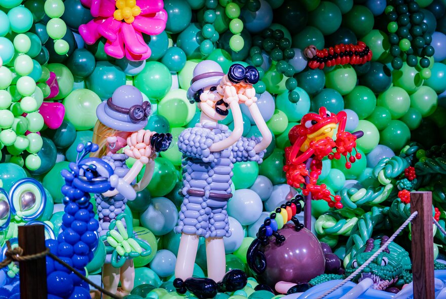 Artwork of figures peering through binoculars in a landscape made of balloons.