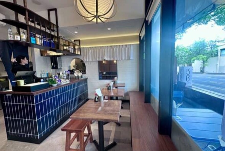 Interior of Kuru restaurant with bench and table seating near the large street facing windows, and a blue tiled service counter.