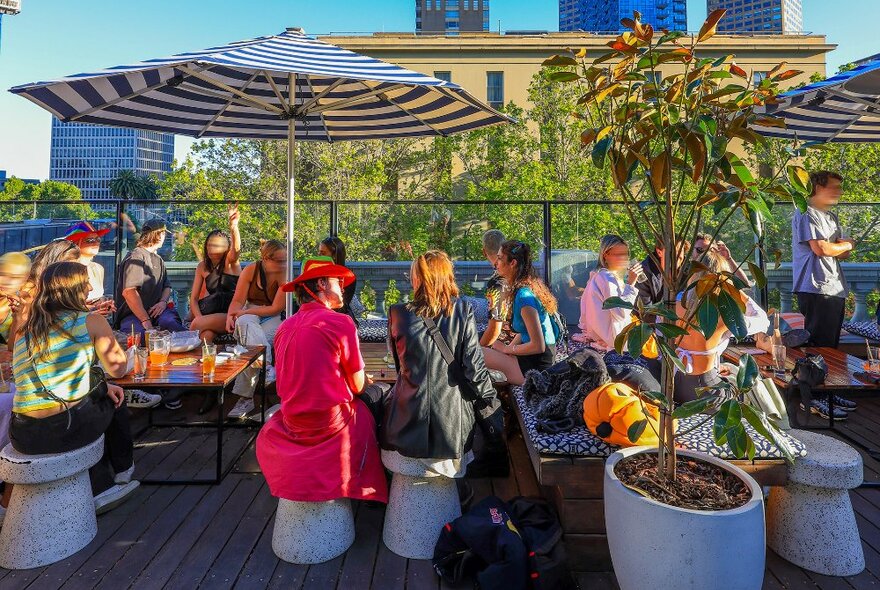 People sitting under stripy umbrellas on a sunny rooftop.