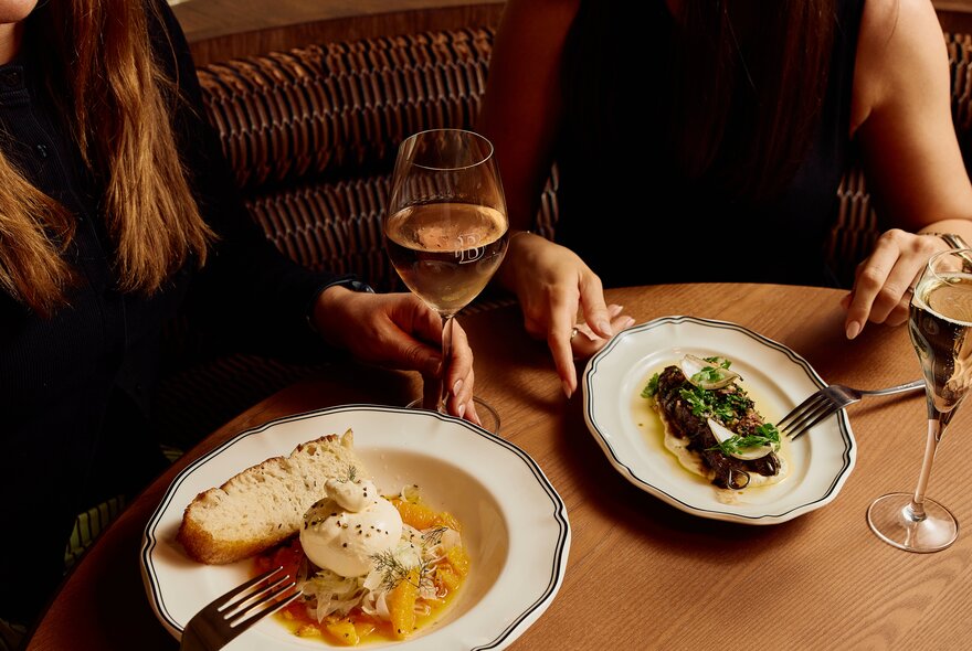 Two diners eating meals and enjoying wine, seen from above.