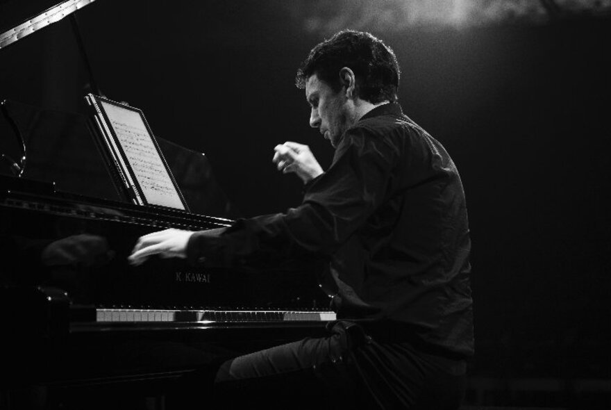 Pianist performing under angled lighting in a dark space.