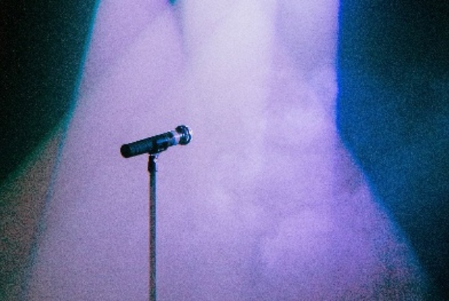 A single microphone stand on a stage under a purple light.