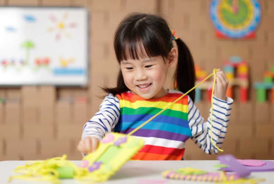 A child gleefully pulling a string on a craft project. 