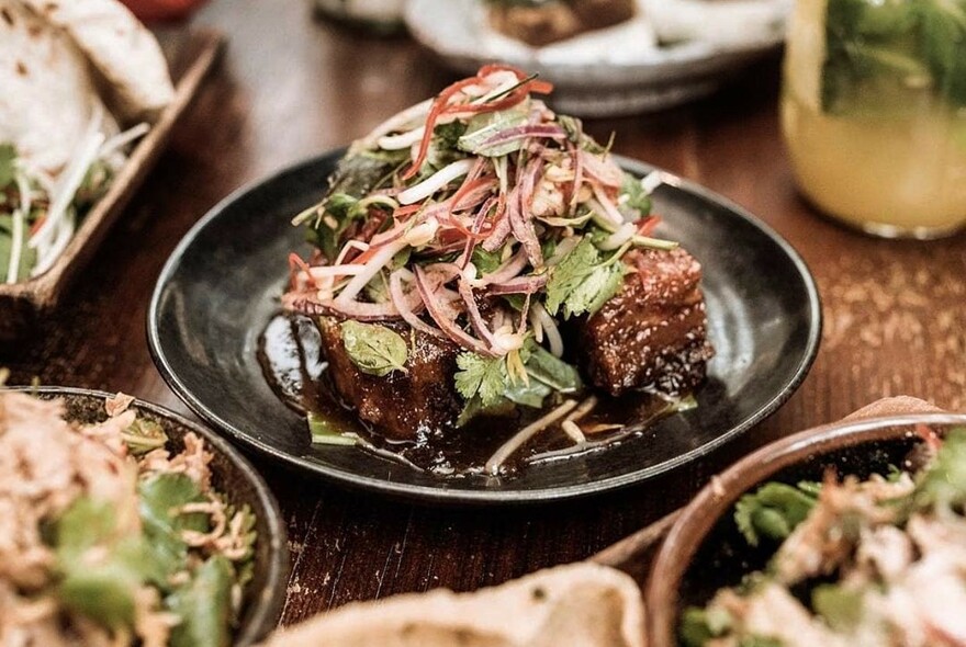 A selection of dishes including salad-topped meat on a black plate.