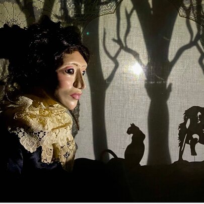 A large puppet head looking to the right of the picture with a silhouette forest with creatures visible. 