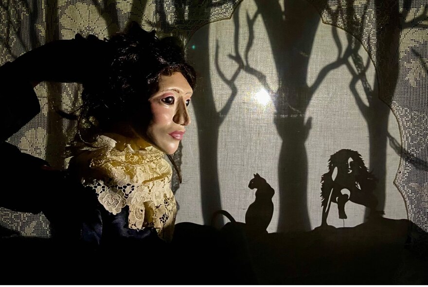 A large puppet head looking to the right of the picture with a silhouette forest with creatures visible. 