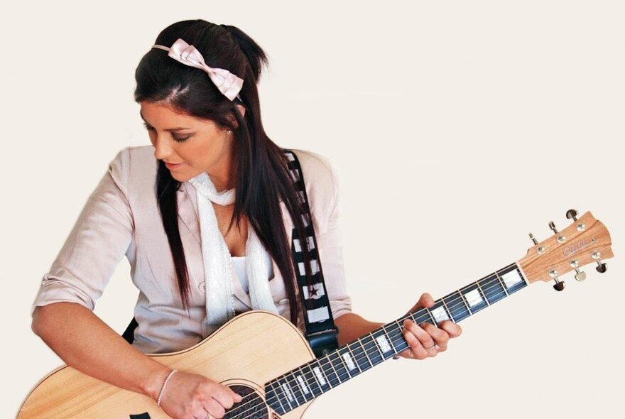 Singer and guitarist Hayley Legg, looking downwards-right with a guitar in her hand and a white bow in her hair. 