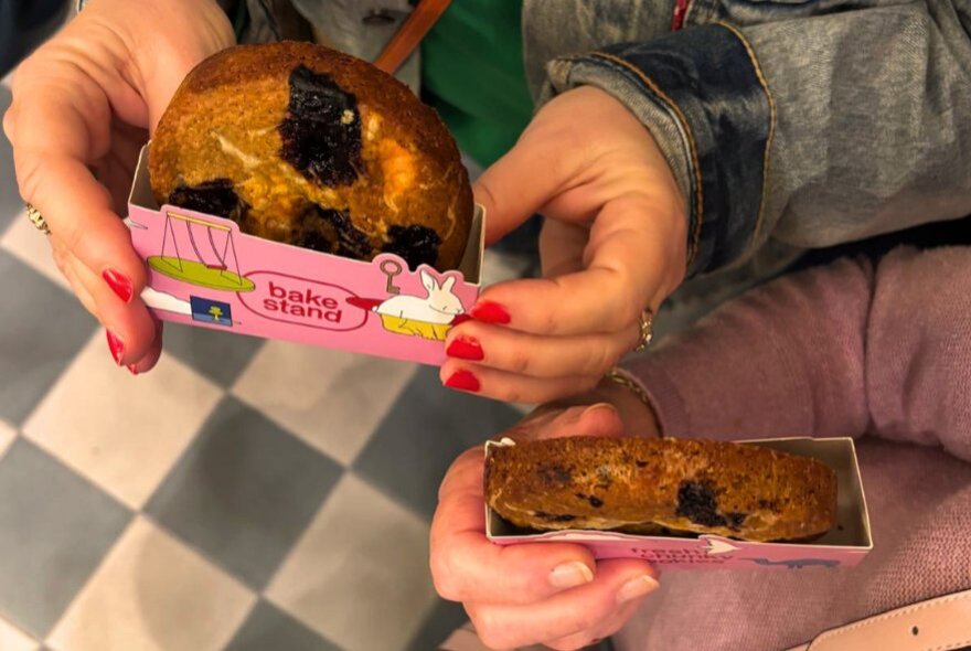 Hands holding pastries in branded packaging.