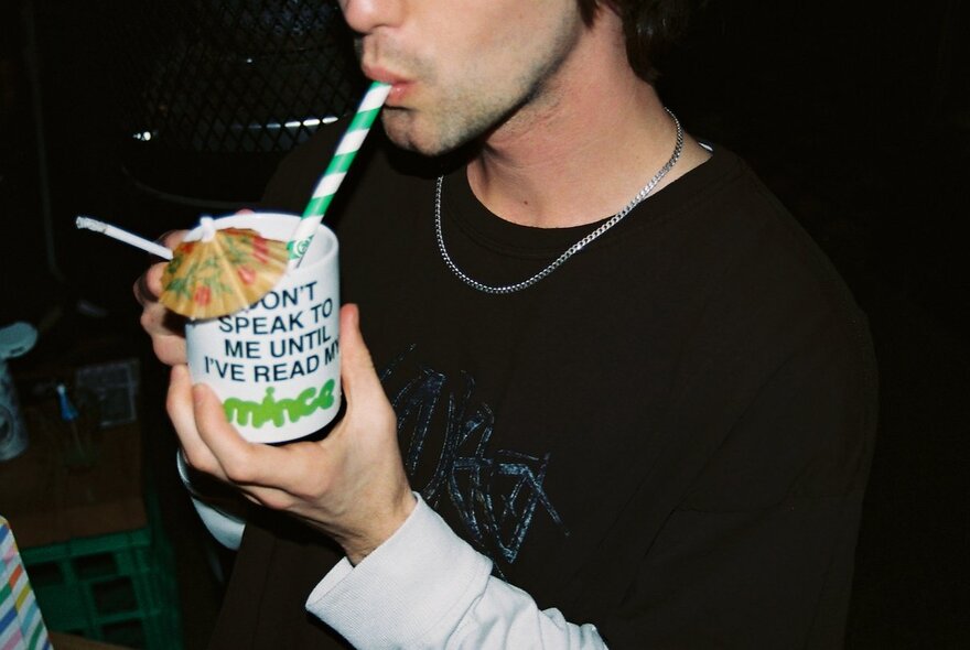 A person drinking something from a slogan mug with a striped straw.