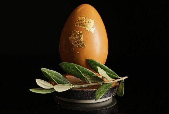 A large caramel chocolate egg with 24 karat gold leaf, resting on a small platter with a sprig of a native Australian bush.