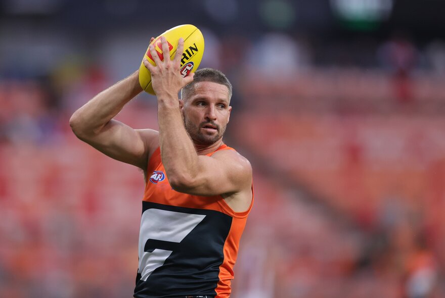 A GWS Giants AFL football player marking the yellow football above his head, on the field during a match.