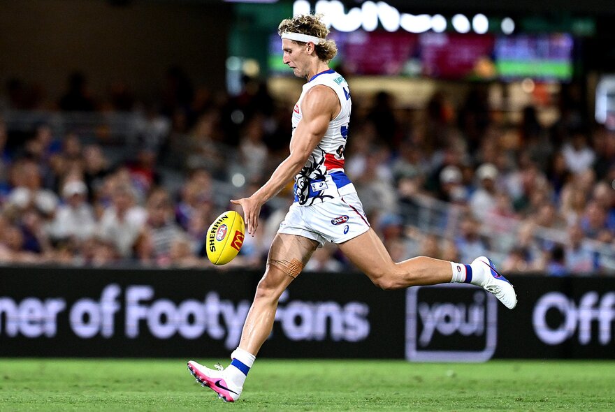 Aaron Naughton kicking a football on the run in a clash jersey in front of a packed crowd. 