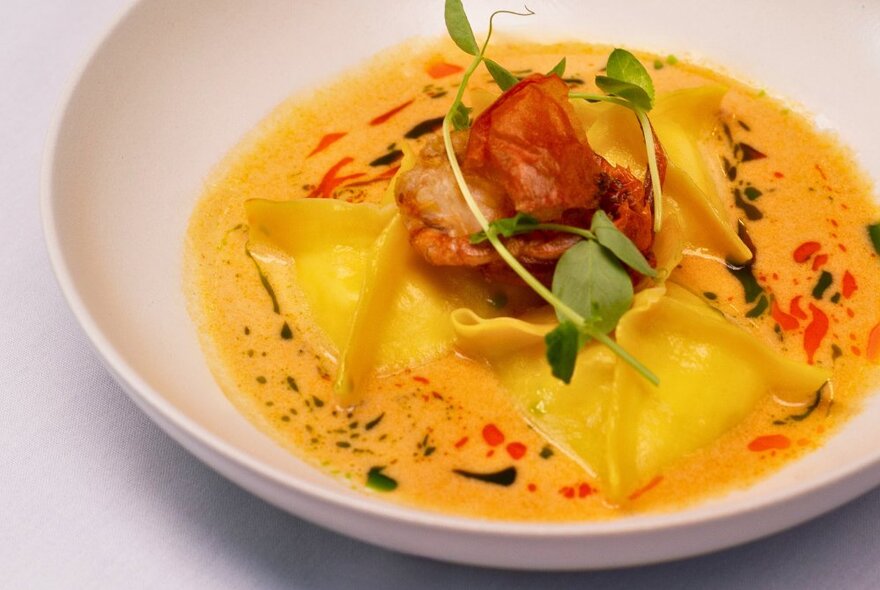 A shallow white bowl with three dumplings in a soupy yellow broth.