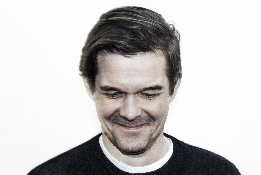 A black and white photo of a a middle-aged man, smiling while looking down.